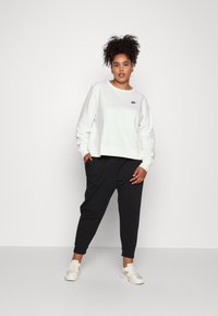 Valkoinen lyhyt tietokonesweatshirt, jossa on pieni musta Nike-logo, yhdistetty mustiin kapeisiin housuihin ja vaaleisiin sneakers-kengiin.