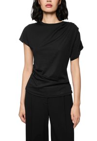 Woman wearing a plain black short-sleeve t-shirt and black pants, standing against a white background.