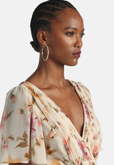 Cvetlična obleka svetlo bež barve z roza in zelenimi vzorci, z razpokanimi rokavi in naborki. Model nosi obročaste uhane.