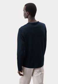 Marineblaues Langarmshirt, Rundhalsausschnitt, weiches Material, lockere Passform, detaillierte Nähte entlang des Kragens und der Ärmelbündchen, getragen mit hellen Hosen.