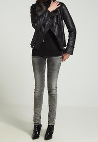 Veste de motard en cuir noir avec col en fourrure, portée sur un haut noir, associée à un jean skinny gris et des bottines noires.