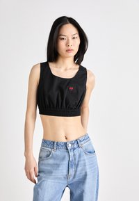 Svart topp med firkantet utringning, elastisk midje og liten rød hjerte-logo. Satt sammen med høyhåndtede lyseblå jeans.