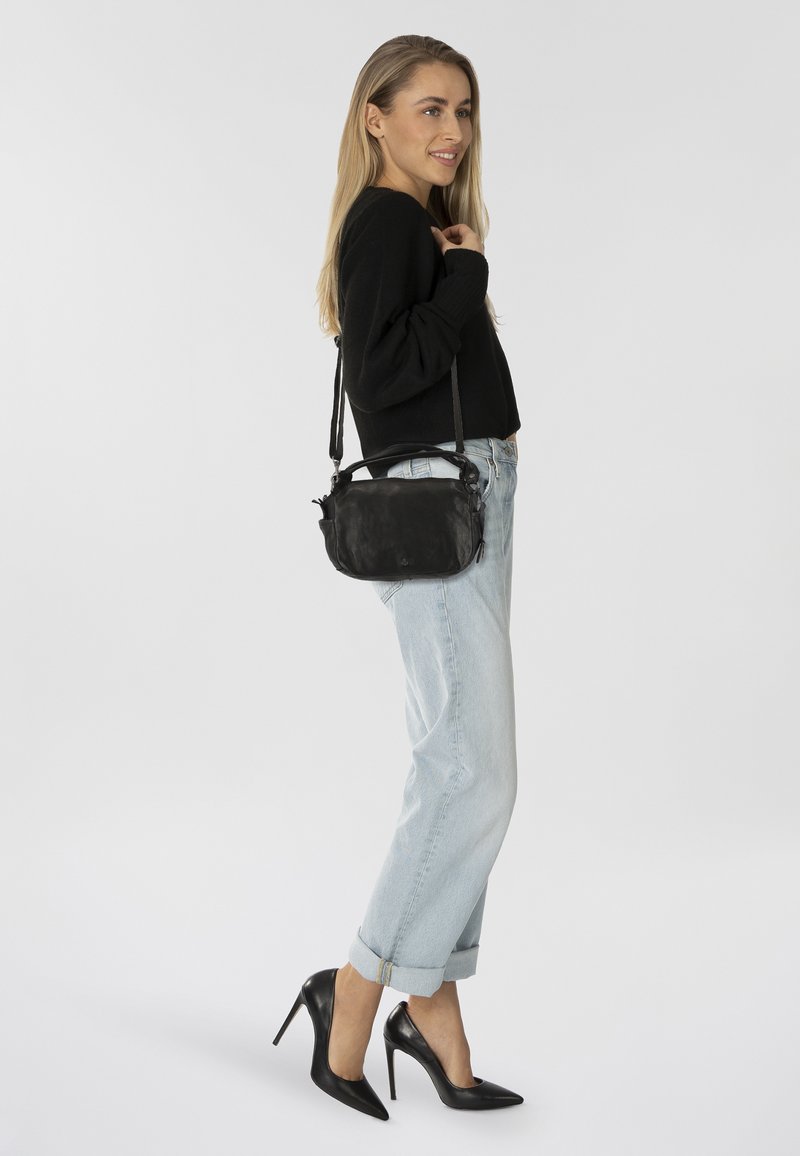 Borsa a tracolla in pelle nera con texture liscia, forma rettangolare, cinturino regolabile e dettaglio della chiusura con zip, indossata da un modello su uno sfondo bianco.