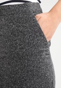 Pantalons en tissu texturé gris avec une petite poche sur le côté droit. Le matériau présente un motif moucheté, ajoutant de l'intérêt visuel.