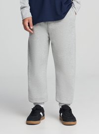 Szare spodnie dresowe z miękkiego materiału, o luźnym kroju z elastycznymi mankietami. W zestawieniu z czarnymi butami sportowymi i granatową koszulą z długim rękawem.