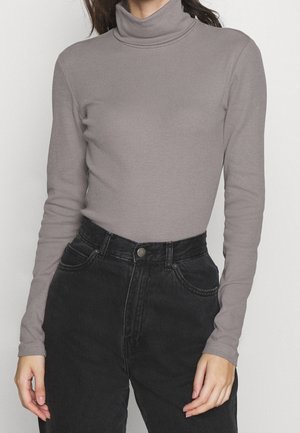 Personne portant un pull gris moulant à col roulé et un jean noir taille haute avec poches avant et fermeture boutonnée.