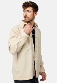 Lys beige button-up skjorte med spredt krave, to brystlommer og en afslappet pasform. Lavet af bomuld, med lange ærmer og en blød tekstur.