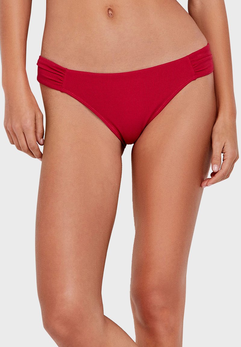 Bas de bikini rouge côtelé avec des détails de fronces sur les côtés et une coupe moyenne. Texture lisse avec des coutures visibles et une taille élastiquée.
