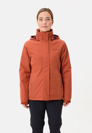 Veste d'extérieur orange avec capuche, fermeture éclair à l'avant et logo. Matériau imperméable, texture lisse et manches longues. Portée sur un pantalon noir.