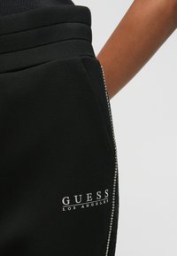 Μαύρο παντελόνι φόρμας από μαλακό ύφασμα, με εκτύπωση λογότυπου και διακοσμητικό φερμουάρ με κρύσταλλα κατά μήκος της ραφής.