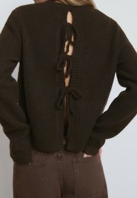 Dunkelbrauner, gestrickter Cardigan mit einer Rückenöffnung, die vier gebundene Akzente und rippierte Kanten aufweist. Weiche Textur und lässiger Schnitt.