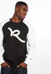 Golf felpa nera con maniche raglan bianche, caratterizzata da un grande logo bianco. Tessuto liscio con colletto rotondo e polsini a costine.