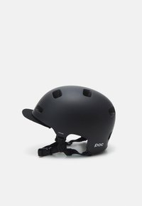 Casco da ciclismo nero opaco con fori di ventilazione, visiera corta, cinturino regolabile e logo sul lato. Texture liscia.