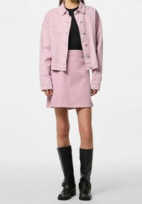 Ljusrosa denimjacka med silverfärgade knappar, tillsammans med en matchande rosa kjol. Svarta knähöga stövlar fulländar outfiten.