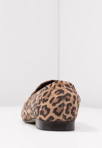 Chaussure plate à imprimé léopard avec un dos arrondi et une semelle noire sur une surface blanche contre un fond gris clair.