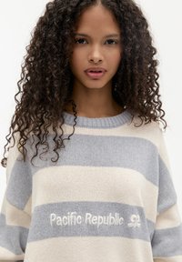 Maglione a righe in grigio chiaro e crema, con logo ricamato "Pacific Republic". Vestibilità comoda con scollatura rotonda.