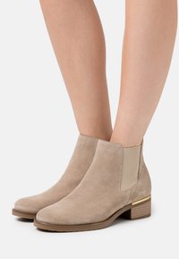 Stivaletti alla caviglia in suede beige con pannelli laterali elasticizzati, punta arrotondata e tacco basso a blocco con un sottile accento dorato.
