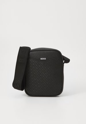 Black crossbody bag with textured pattern, front logo, and adjustable strap. Rectangular shape with curved top and zipper closure.