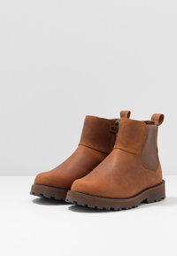 Bottines en cuir marron avec des panneaux latéraux élastiques, un dessus texturé et une semelle en caoutchouc robuste pour une meilleure adhérence et durabilité.