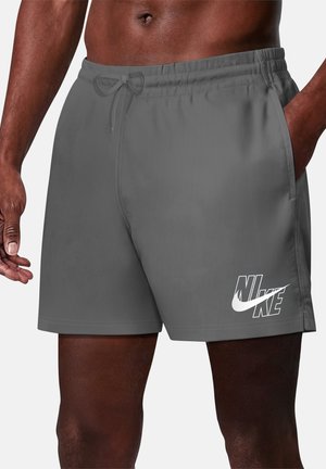 Uomo che indossa pantaloncini Nike grigi con vita con coulisse e tasche laterali, che mostra il logo vicino alla coscia sinistra su sfondo uniforme.