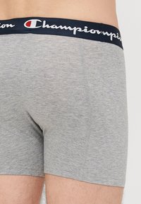 Shorts de boxer gris avec une taille marine ornée du logo "Champion" en blanc. Tissu doux, design ajusté et coutures plates pour un confort optimal.