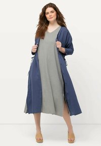 Długi, granatowy kaftan w stylu kimono wykonany z miękkiego materiału, nałożony na jasnoszary, luźny fason sukienki, uzupełniony o beżowe espadryle.