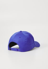 Lila basebollkeps med strukturerad tyg, böjd skärm och plastsnäppstängning. Har ventilationshål på sidorna.