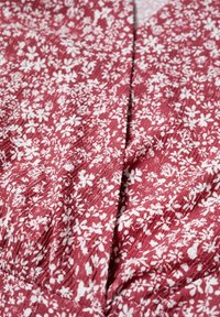 Tkanina sukienki w kwiaty w głębokim czerwonym kolorze z małymi białymi kwiatami. Zmięta tekstura i plisowany wzór, tworzące wizualne zainteresowanie i ruch.