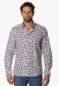 Camisa blanca con un patrón circular negro, cuello abotonado, corte ajustado y mangas largas. Tejido suave con botones en contraste.