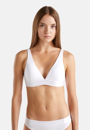 Bralette blanche avec un design en V, fabriquée en tissu lisse. Possède de larges bretelles et une bande logo. Construction simple et sans couture.