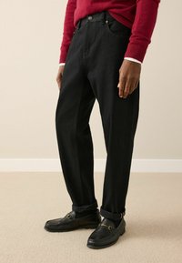 Black denim trousers with a straight-fit design, featuring five pockets and a button and zipper closure. Paired with black loafers.