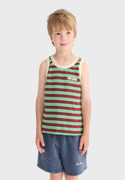 Garçon blond debout, portant un débardeur rayé vert et bordeaux et un short bleu, les deux avec le logo "Bobo Choses".