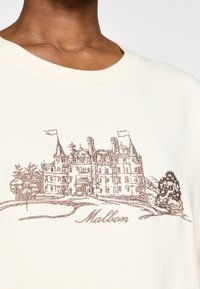Sudadera color crema con ilustración bordada en marrón de una mansión y árboles, con el texto "Malbon" debajo. Cuello redondo.