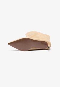Beige suede ankle boot with a pointed toe, textured surface, and a slim brown heel. Flat outsole with subtle traction grooves.