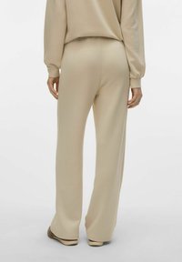 Pantaloni beige a gamba larga realizzati in tessuto morbido; presentano una texture liscia e una vita elastica. L'orlo è leggermente arrotondato in fondo.