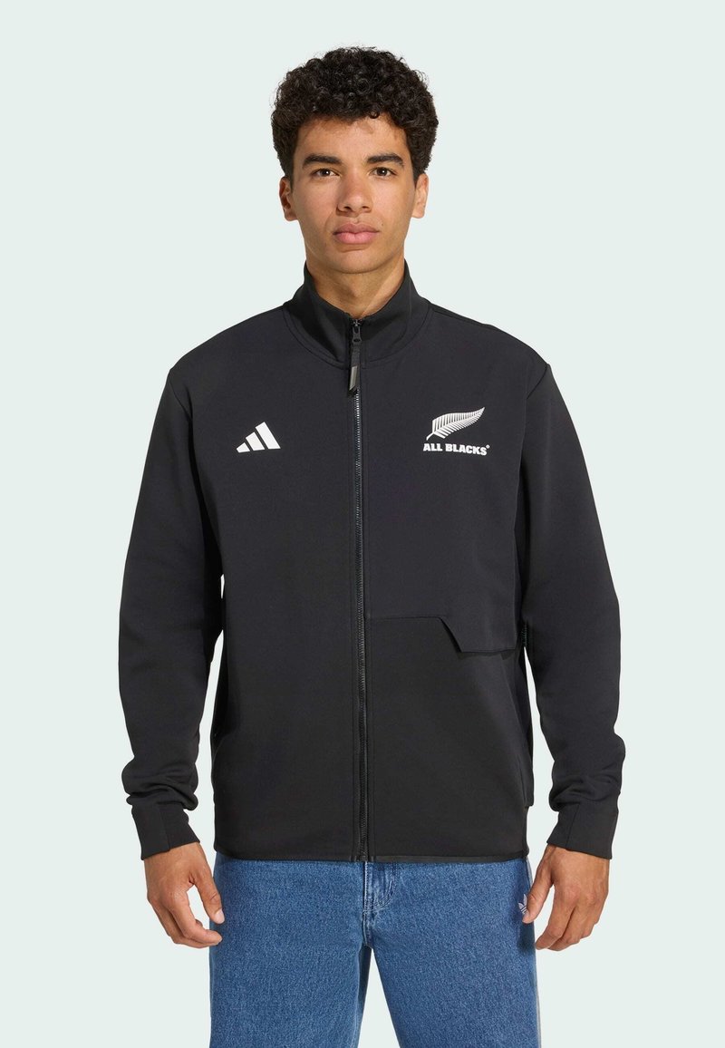 Sort sportjakke med høj krave, fuld lynlås, Adidas-logo, All Blacks-emblem og lomme detaljer. Lavet af glat, strækbart stof.