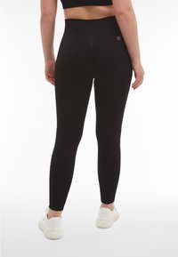 Leggings neri a vita alta con una texture liscia e design aderente, con dettaglio logo sulla parte posteriore e taglio alla caviglia.