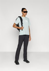 Ανοιχτό πράσινο μπλουζάκι με λευκό λογότυπο, μαύρο σακίδιο, σκούρο παντελόνι και μαύρα παπούτσια. Στρογγυλά γυαλιά ηλίου ολοκληρώνουν την εμφάνιση για εξωτερικούς χώρους.