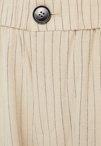 Tejido beige con rayas verticales negras, que presenta un botón negro y una superficie texturada sutil. Vista en primer plano del detalle de la prenda.