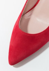 Gros plan d'une chaussure plate pour femme en daim rouge à bout pointu avec une doublure intérieure beige.