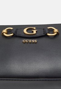 Černá kožená kabelka se zlatými detaily, vybavená vysoce viditelným zlatým logem "G" a nastavitelným popruhem. Hladká textura a minimalistický design.