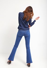 Mörk denimskjorta, lång ärm, åtsittande design. Blå utsvängda jeans, medelhög midja, med bakfickor. Bruna klackskor med tjock klack.
