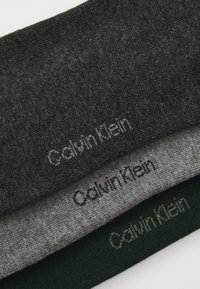 Három hajtogatott Calvin Klein zokni sötétszürkéből, világosszürkéből és sötétzöldből, mindegyiken a márkanevével hímezték a szélénél.