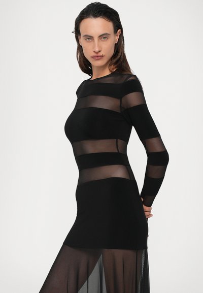 Črna obleka z polprosojnimi mrežastimi črtami, dolgimi rokavi, oprijetim korpusom in široko krilo s stranskim razporkom.