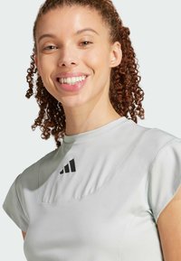 Heledane hallhalli särgid, lühikeste varrukatega, ümarate kaelustega ning musta Adidas logo rinnal. Sile, veniv kangas.