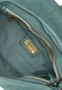 Interno di una borsa in pelle teal con una cerniera dorata, foderata in tessuto e un'etichetta del marchio contrassegnata "CATERINA LUCCHI, MADE IN ITALY."