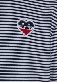 Pasiasty bawełniany top w kolorze granatowym i białym, z naszywką w kształcie serca wykonaną w kolorach czerwonym, czarnym i białym oraz napisem "TOMMY."