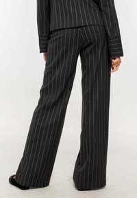 Pantalones a rayas negros con corte entallado, que presentan un diseño de pierna ancha y una tela texturizada; brillo sutil de los acentos de hilo metálico.