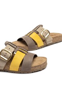 Suede sandals with brown, yellow, and beige straps, featuring a gold buckle and textured cork footbed. Rounded shape and flexible sole.