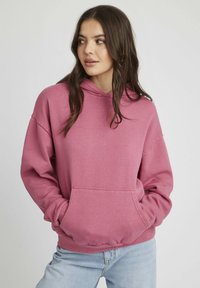 Hoodie rose avec un capuchon à cordon, une poche avant et des poignets côtelés. Fait en tissu doux, il offre une coupe décontractée et une texture lisse.
